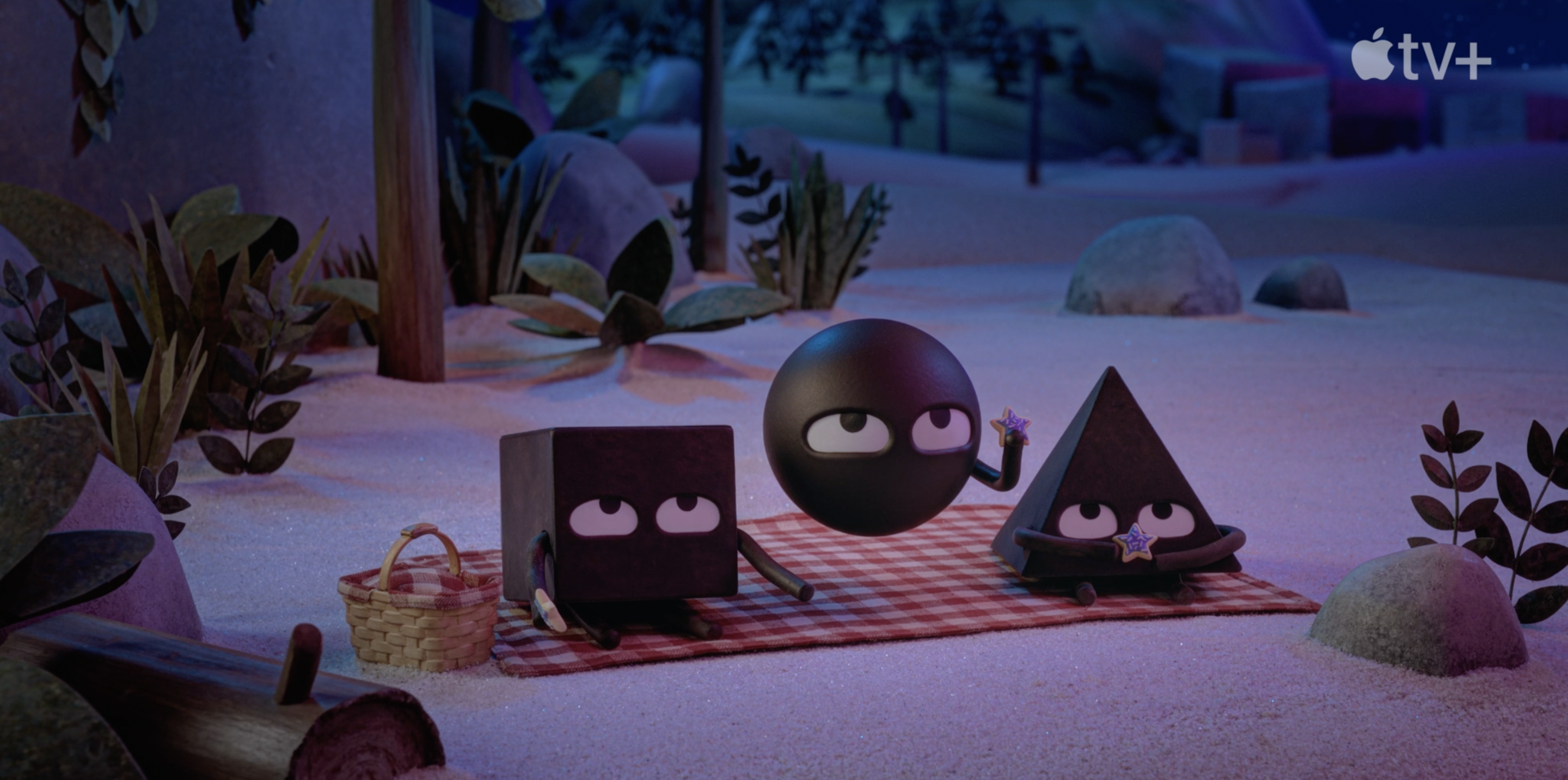 A screenshot from The Shooting Star. Square, a Circle, and a Triangle sit on a picnic blanket on a moonlit beach . They hold star cookies and gaze upward at something unseen.